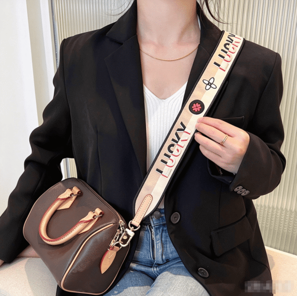 lucky-canvas-shoulder-strap-speedy-casual-outfit Woman wearing black blazer with Speedy handbag and decorative “LUCKY” canvas shoulder strap, casual chic daily outfit, stylish crossbody look.